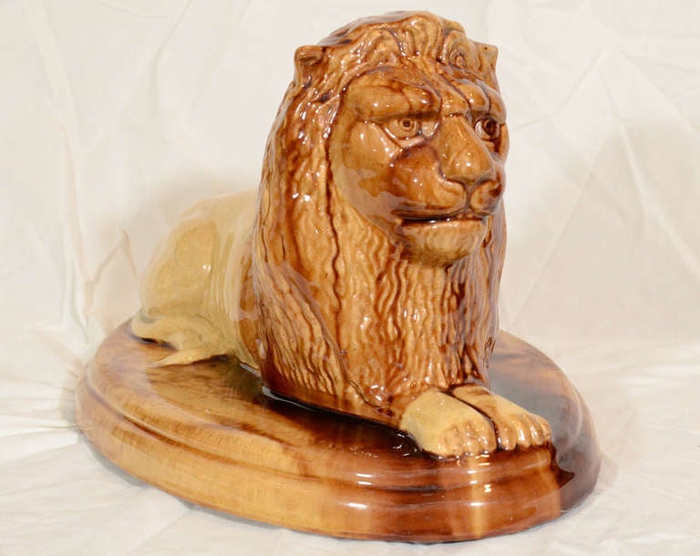 A yelloware figure of a recumbent lion with its tail curled to the side, above an oval base, the mane incised in brown and cream glaze. Made in East Liverpool, Ohio which during the 19th century was known as the pottery capital of America. In 1839