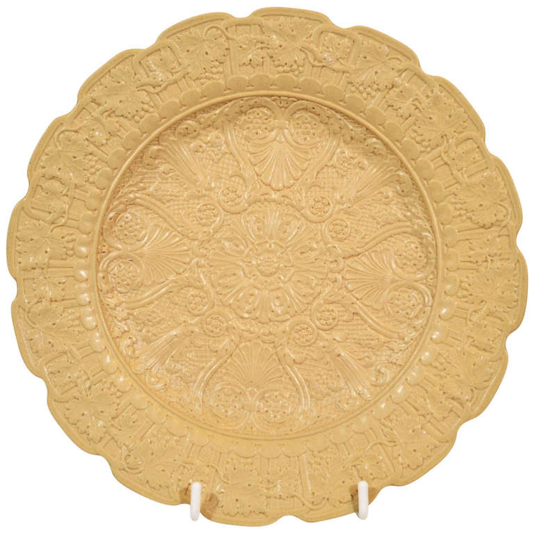 Each drabware plate is impressed with a raised design of palmettes around a central rondel. A wide border of grape leaves and a lobed edge finish the design.