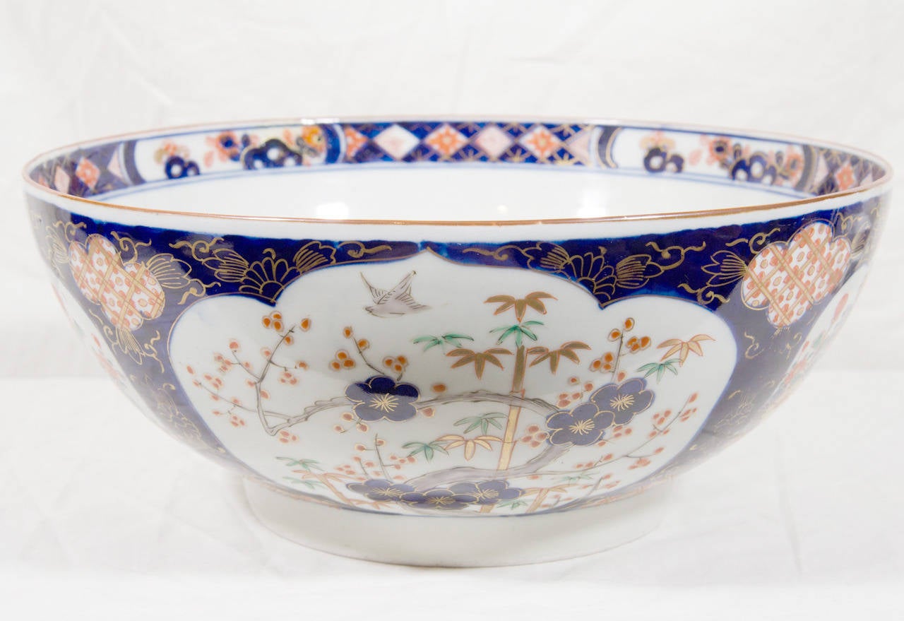 A Japanese Imari bowl painted in cobalt blue, red, green and gilt. The outside is decorated with a profusion of flowers in cartouches. The well is decorated with a traditional garden scene. Export of Imari Porcelain to Europe surged in the Meiji Era
