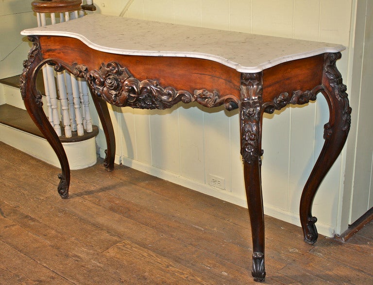 An 'Anglo-Indian' export hand-carved solid rosewood and mixed hardwood reverse serpentine console or serving table;  with a conforming turret cornered Ogee edged Carrara marble top.  Made for export to Europe, at the outset of the reign of Queen