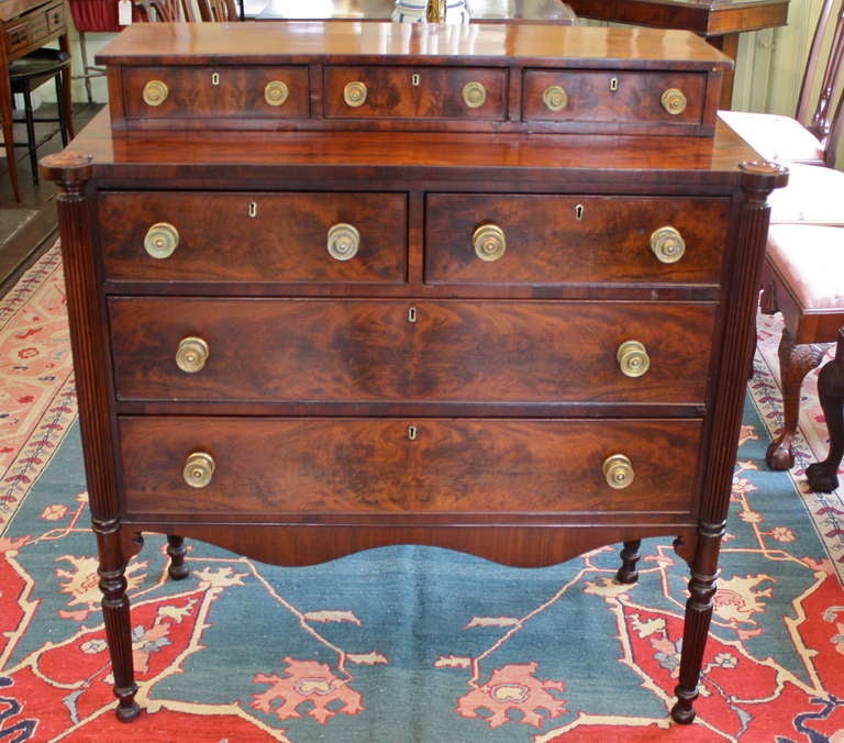 In the Sheraton manner, a fine crotch mahogany staged or 'stepback' chest of drawers.   Reeded turret-cornered chest of four case drawers and three small stage drawers; raised on four ring turned and reeded legs with intervening scalloped aprons.