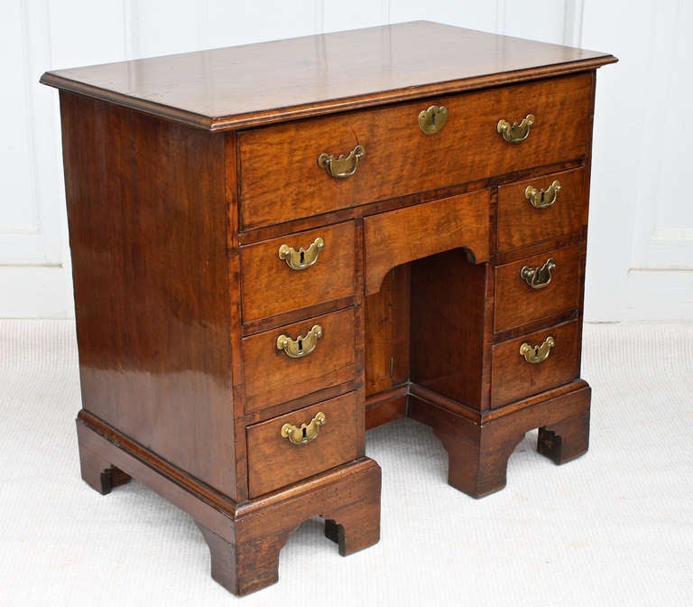 A diminutive early Georgian kneehole desk, with one large and seven smaller drawers, and the prerequisite recessed kneehole cabinet.  The walnut is attractively grained, marred and patinated.  It is raised on a stepped arched bracket-footed base;