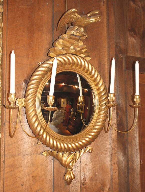 A nautical rope-twist carved gilt wood convex mirror, with an American Eagle landing on a rock ledge and oak leaf foliate carved pendant.  FOUR c-scroll candle arms with carved gilt wood candle cups and bobeches.  Rare and unusual in its less formal