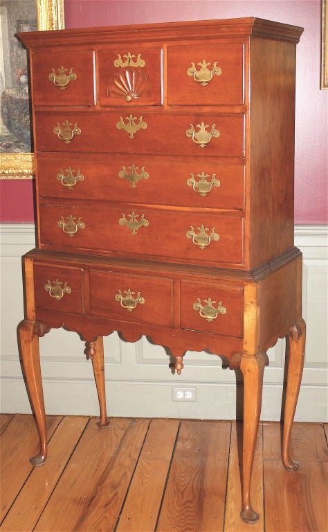 An early flat-topped slightly diminutive high chest (chest of six drawers on a three drawer stand).  The cherry case of two parts features a FAN CARVED top center drawer, a shaped apron, finial drops, and proportionately tall slender Queen Anne
