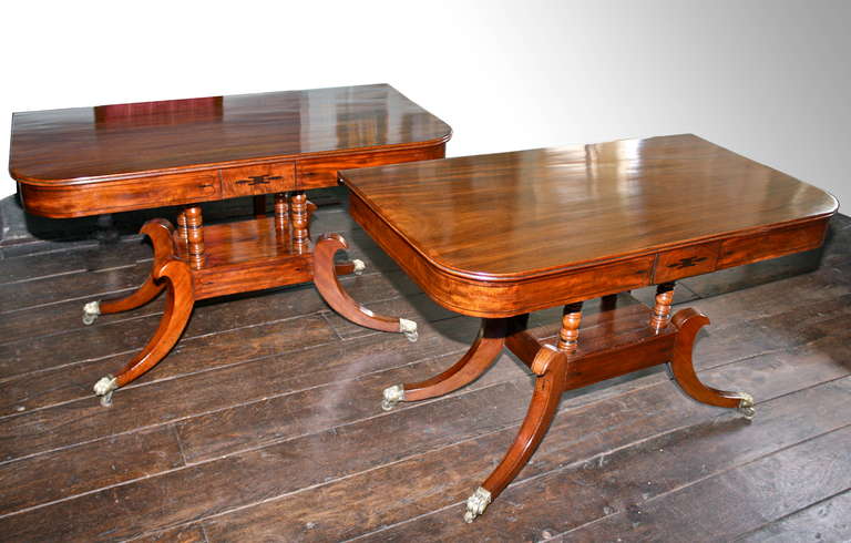 An English Regency period pair of ebony inlaid and vividly grained mahogany consoles; each on four kneed saber legs, footed in brass paw casters.  Purposely 'metamorphic', the consoles can be joined together by inserting two matched leaves; 