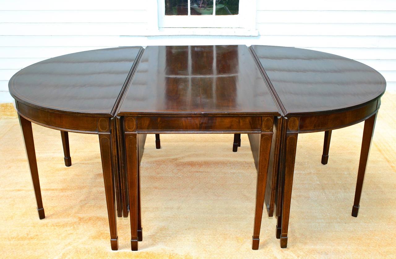 A tripartite very finely inlaid mahogany banquet table in the Hepplewhite manner, comfortably seating 12. Its two demilune ends with drop leaves may also be joined without the center drop leaf section, to seat six. The center drop leaf table may be