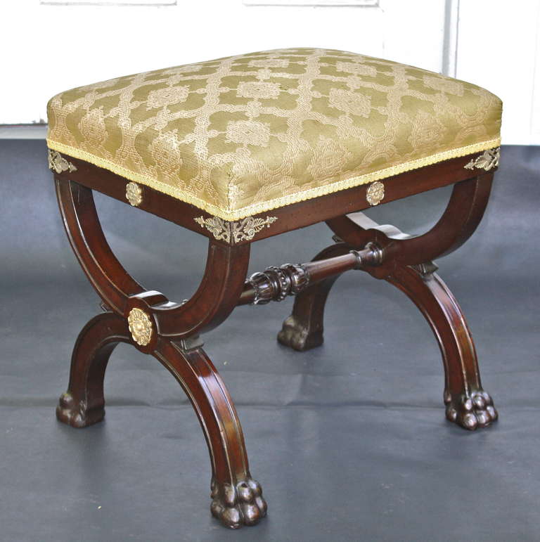 A neo-classical mahogany curule tabouret or stool with gilt bronze mounts, lion paw feet, and attached box-upholstered seat.  Oak secondary woods suggest English origin.  Hand-carved decoration to the turned stretcher, as well as overall structural