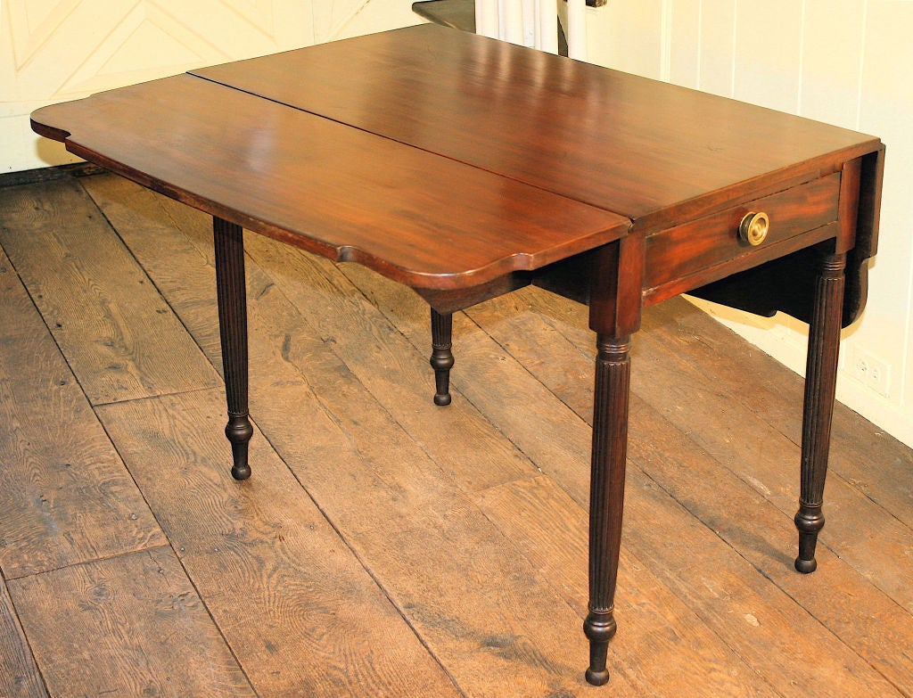 Of dark grained mahogany in its original finish, an oversized reeded leg Pembroke table with distinctive cut corners, and an apron drawer with original brass pull.  With Sheraton stylistic references, it was likely made in the Vesey Street NYC shop