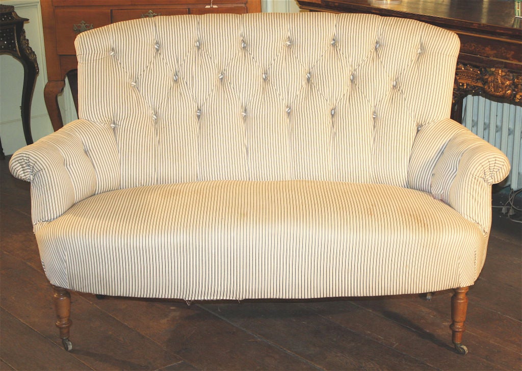 A two-seater upholstered settee, with button-tufting, raised on turned front and plain rear legs; all on wooden casters.  Provenance: Shelton, Mindel, NYC.
