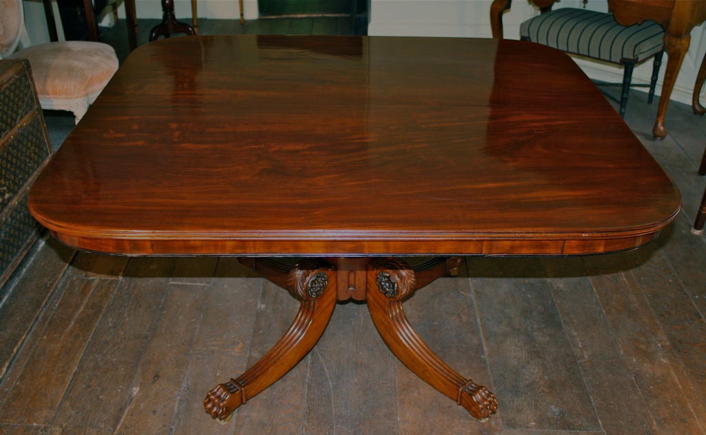 A hand planed, hand turned, and ornately hand carved solid mahogany tilt-top center, breakfast, or small ancillary dining table for four.  On four foliate and reed carved legs, ending in hand carved mahogany lion's paw feet on brass casters; the