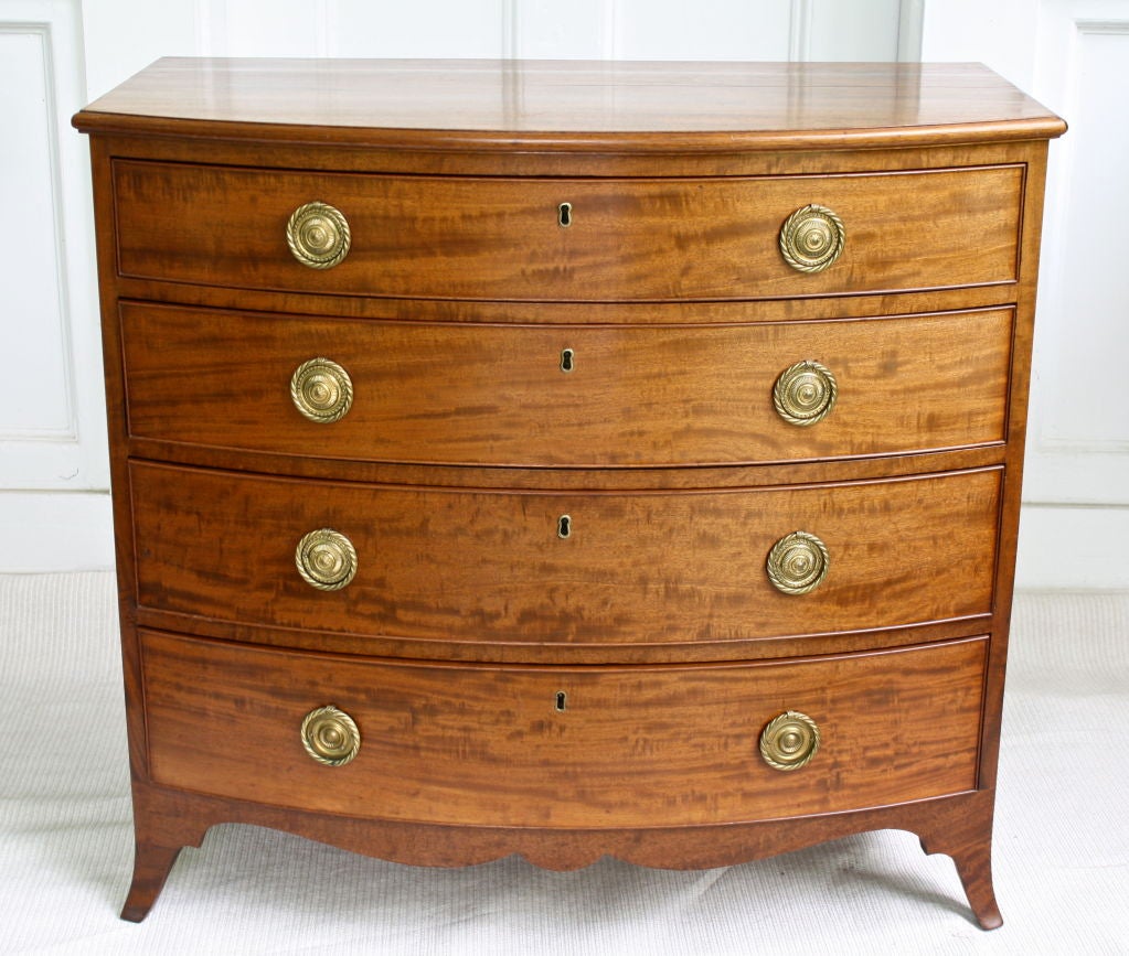 A Scottish bowfront bureau of four graduated drawers, made of  figured light mahogany; raised on splayed French feet with scalloped aprons.  Original mellow finish and patina, with period twist ring brasses.  Its case is of a slightly smaller scale.