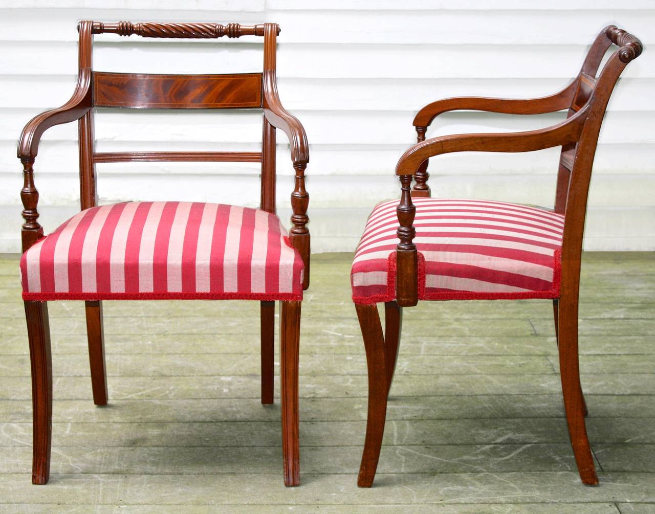 In the manner of Thomas Sheraton (1751-1806), two armchairs and six side chairs all of the same crest rail height.  Hand-carved and hand-turned mahogany, with box upholstered seating and sabre legs.  Crotch mahogany veneered horizontal back panels,