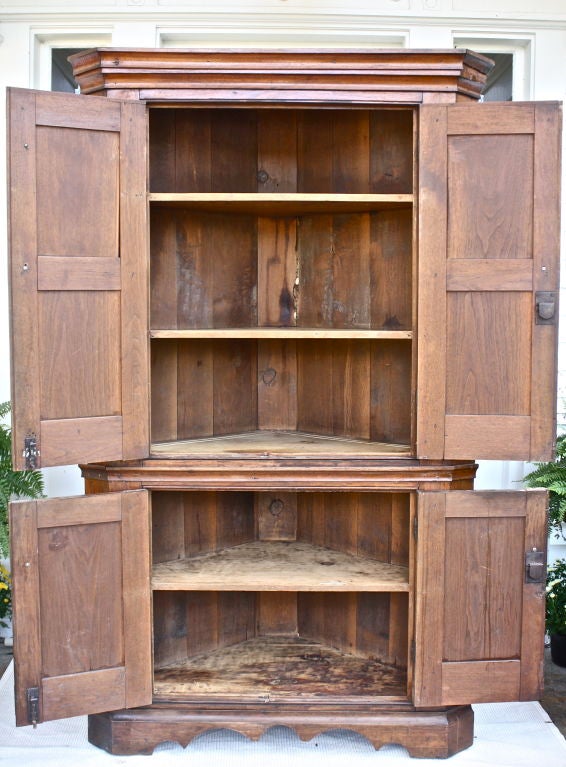 Walnut corner cupboard in two pieces; with four panelled doors concealing three shelves in the upper cabinet and two in the lower.  Bracket footed, scalloped frieze base. Turned walnut door pulls. Very old and possibly original surface.  Scalloped