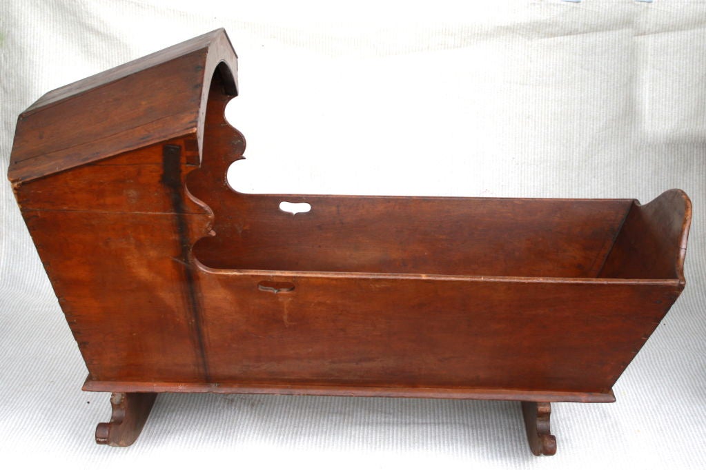 Of cherrywood in its original old red wash, with graceful scalloped flourishes and corner dovetailing;  a child's cradle in the Moravian manner.  There is an old metal brace on just the right side, level with the hood facing.