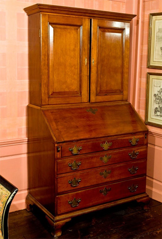 A cherrywood slant-front secretary on ogee bracket feet, with a complex blocked and fan carved interior, multiple drawers and pigeon holes, and a ledger recess. Two upper case panel doors enclose three fixed shelves. The lower case contains four