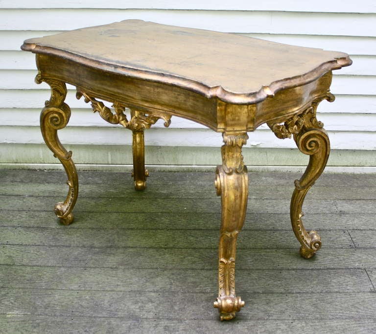 A Florentine Baroque period rectangular turret-cornered gilded center table or console, raised on four ornately scrolled legs.  Its friezes are decorated with suspended foliate garlands.  A true 'center table', visually perfect on all four sides; or