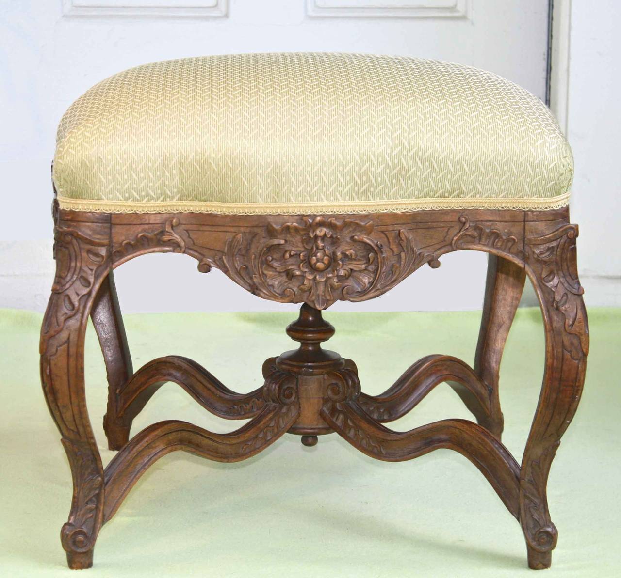In the style of Louis XV, an ornately carved square French Court tabouret or footstool, with finial mounted cross-stretchers.  Ex: collection of actor Jason Robards at Southport, Connecticut.
