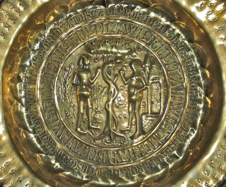 A Germanic Renaissance Period embossed brass shallow basin for the ecclesiastical collection of alms.  The Tree of Life depiction of the temptation of Adam by Eve is surrounded by not just one, but two concentric circular inscriptions in Old German.