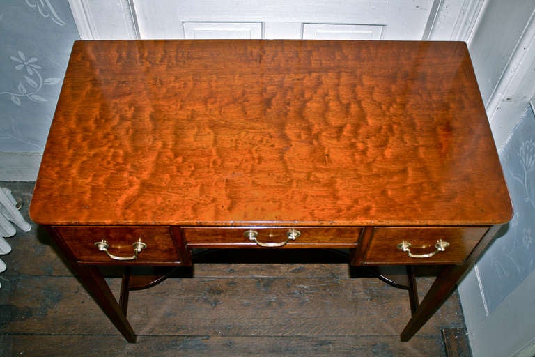 George III period Hepplewhite manner specimen 'plum pudding' and flame figured mahogany three drawer serving console; with stretcher-level galleried shelf.  Original brasses.  Stair and Company (New York) warranty plaque attached in the right
