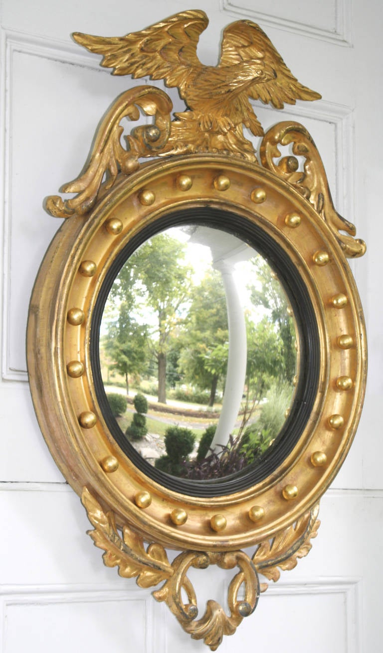 A Federal period giltwood convex 'bulls eye' mirror, surmounted by a hand-carved American eagle, with pierced-carved foliate pediment and pendant.  The oak foliate pediment and pendant are Philadelphian Chippendale design elements in mirrors;