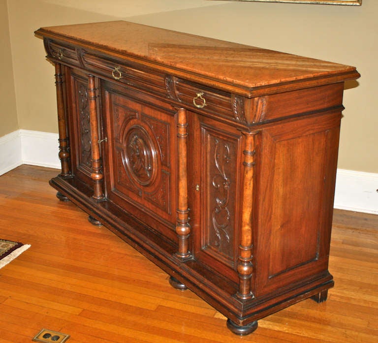 An American Renaissance Revival columned and plaqued,  3 doored and 3 drawered, panel-ended cabinet; raised on bun feet.  An original terra-cotta colored marble top is inset.  Each lockable door conceals three levels of shelving.  Unusual brass