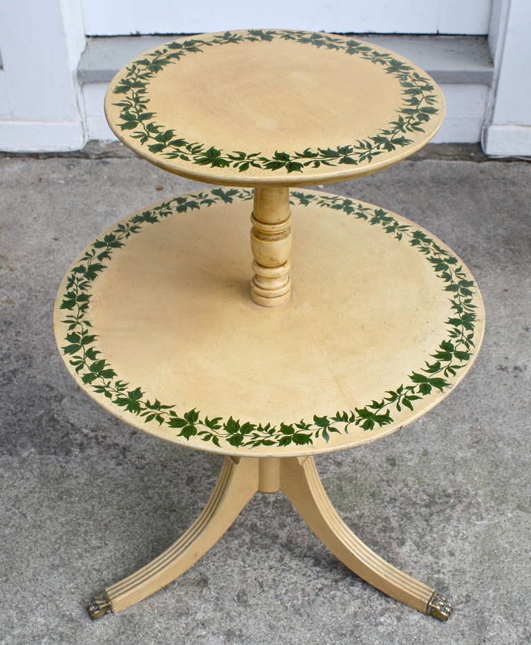 An ivy stenciled two tiered tripod dumbwaiter of smaller scale, with brass paw capped feet.  Its structure is nicely turned and carved; though clearly machine age and not of the period.  The paint decoration has been attributed by narrative to the