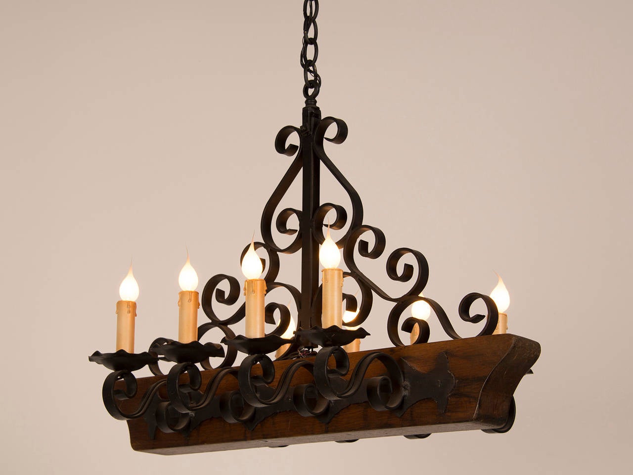 A decorative chandelier from France c. 1950 featuring a shaped wooden beam having an iron assembly of four iron candle arms on each side for a total of eight lights. This fixture is suspended from a beautiful piece of iron scroll work and has