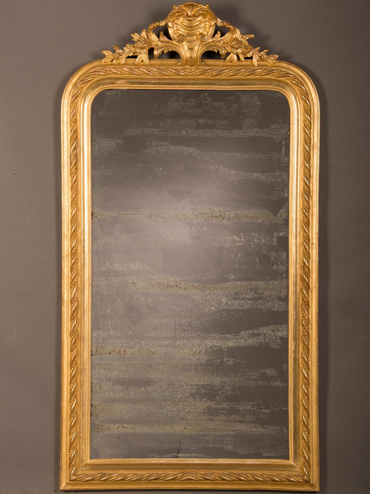 A Louis Philippe style gold leaf frame surrounding the original mirror glass from France circa 1885. This exceptional mirror and frame showcase a wonderful contrast between the decorative nature of the frame and the fantastic aspect of the aged and
