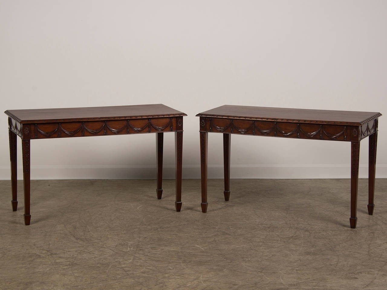 A pair of Adam style carved mahogany console tables from England c. 1850. Please notice the handsome carved details on each of these tables. The placement of the carving is visible not only from the front but also on each of the sides. Not only is