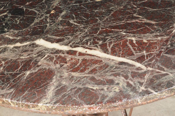 A wonderful iron base dining table with a marble top from France c. 1890. The iron base has a lovely decorative appeal with four scrolled feet that move inward and upward to enclose a pattern of opposing scrolls. Please note that each of these four