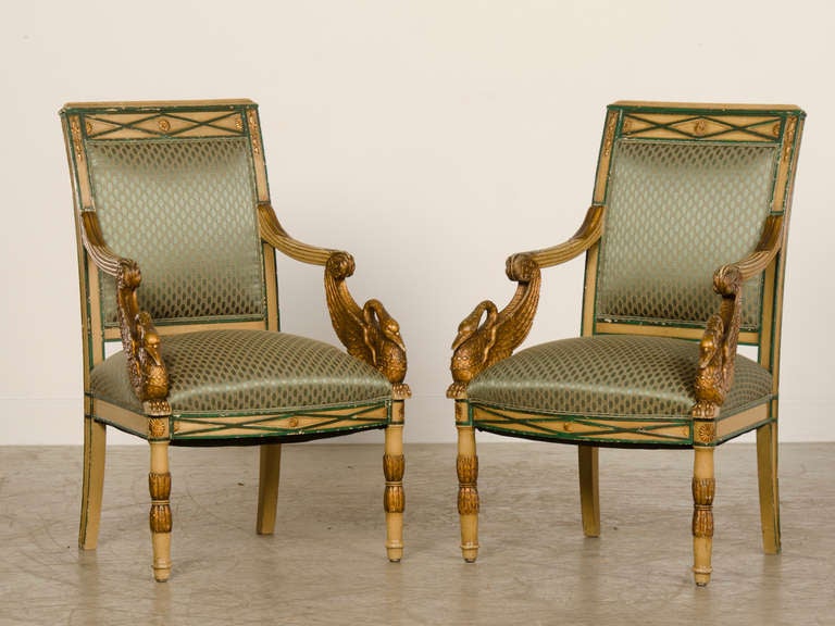 A pair of Empire period painted and gilded arm chairs from France c.1810 featuring swan heads with exceptional carving. These armchairs or 