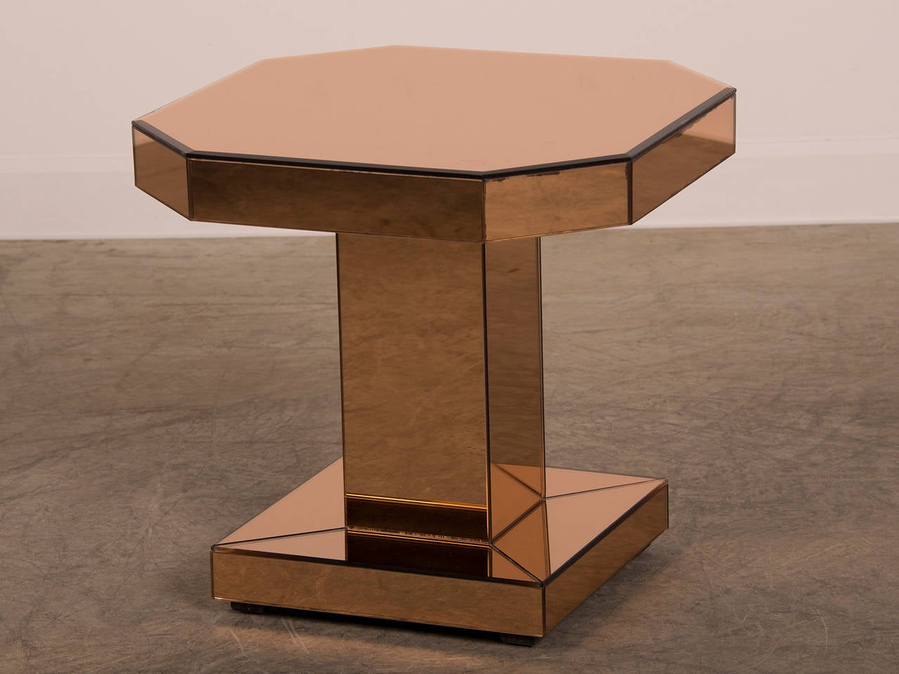 An Art Moderne side table with an octagonal shape standing upon a square pedestal and base entirely sheathed in bronzed mirror glass from France, circa 1940.