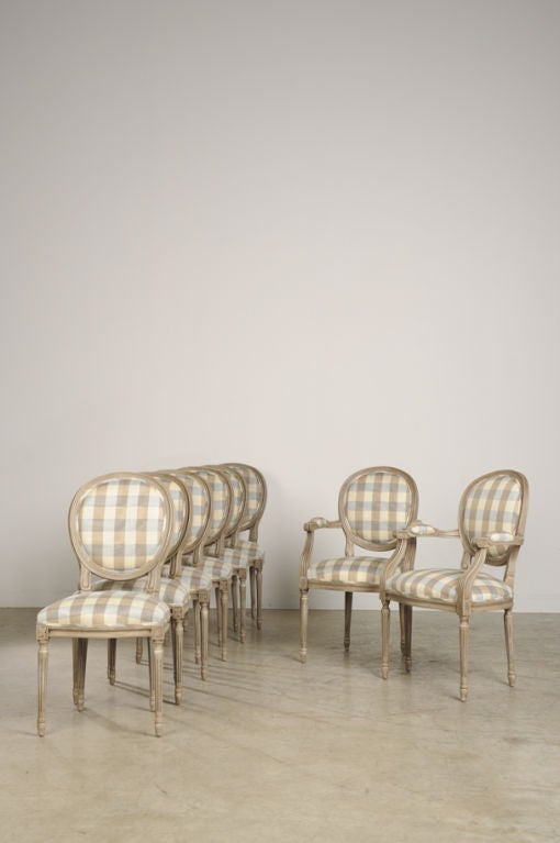 A set of oval back Louis XVI style dining chairs with a painted finish from France now custom upholstered in a charming taupe and French blue plaid. Please notice the elegant restraint of the shape with a minimum amount of carved detail. This set of