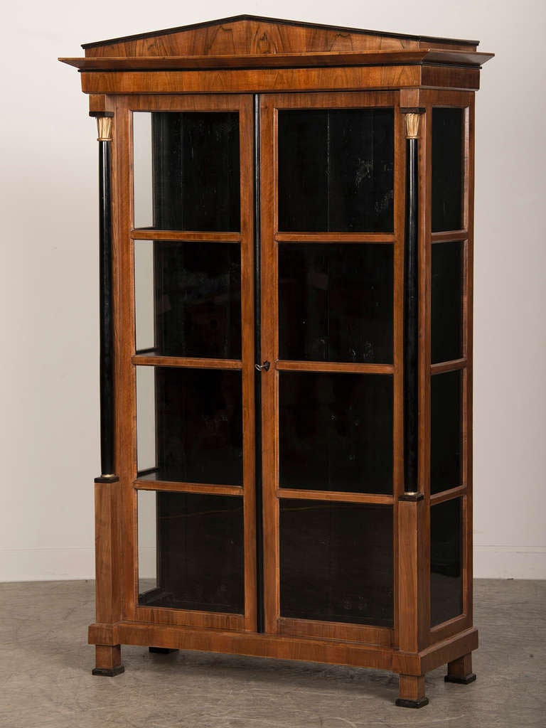 An elegant Empire style walnut vitrine from Austria c. 1890 with three shelves and having ebonized wood columns and trim detail with glass panels on the front and sides.