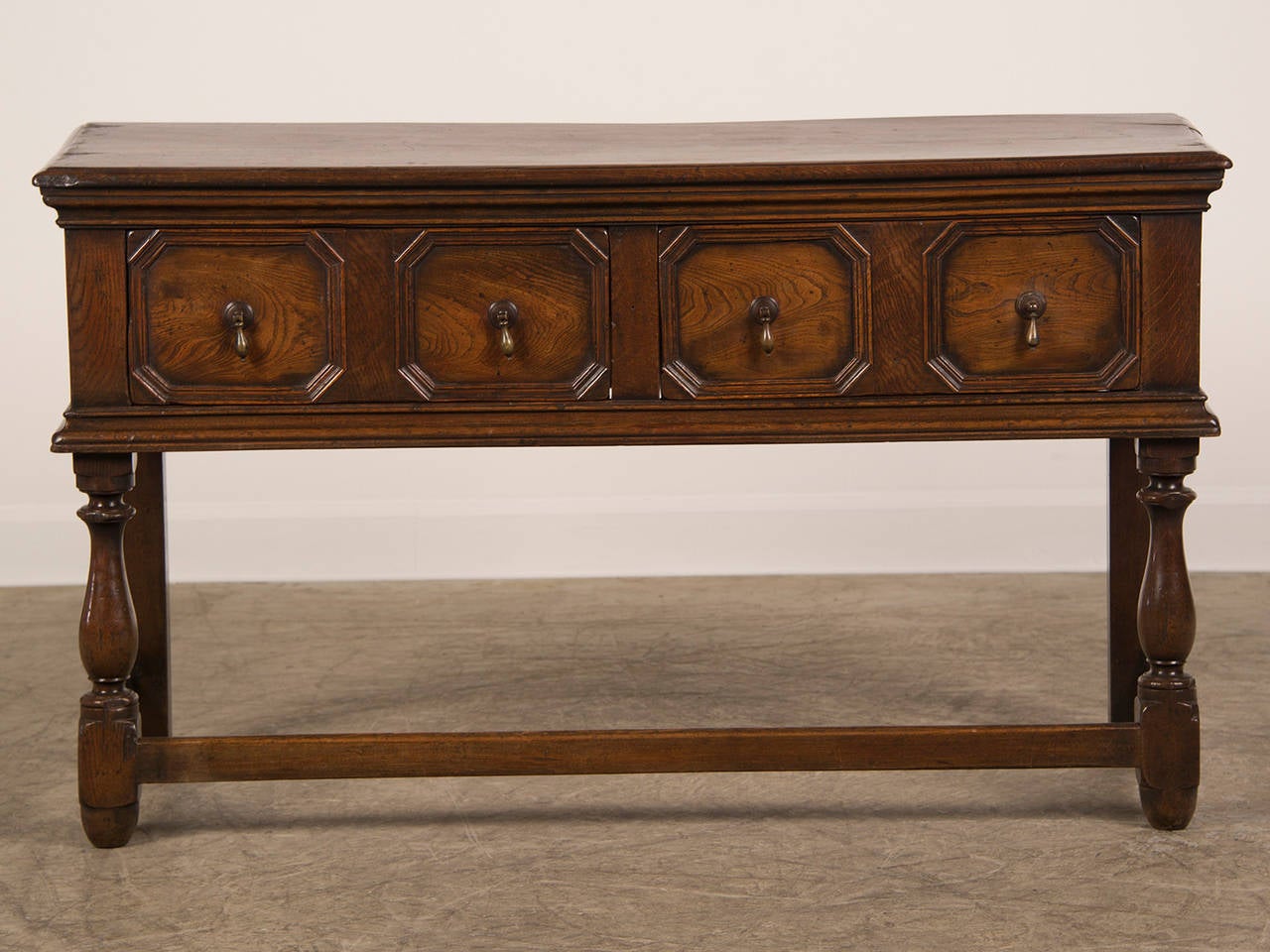 A Jacobean Revival oak serving table from England c. 1885 having two drawers. Please notice the strong geometric quality of the symmetrical drawer fronts to this piece. Each octagon is framed by a deep moulding and is centred on a brass drop pull.