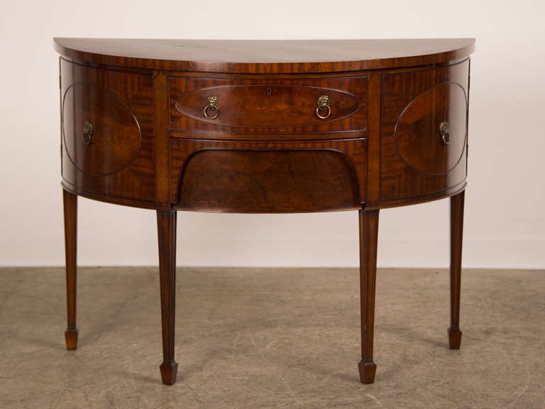 A Sheraton style mahogany demi-lune console sideboard from England c.1880. The shape of this cabinet is most unusual and gives it a definite allure when choosing it to place within an interior. The shape, 