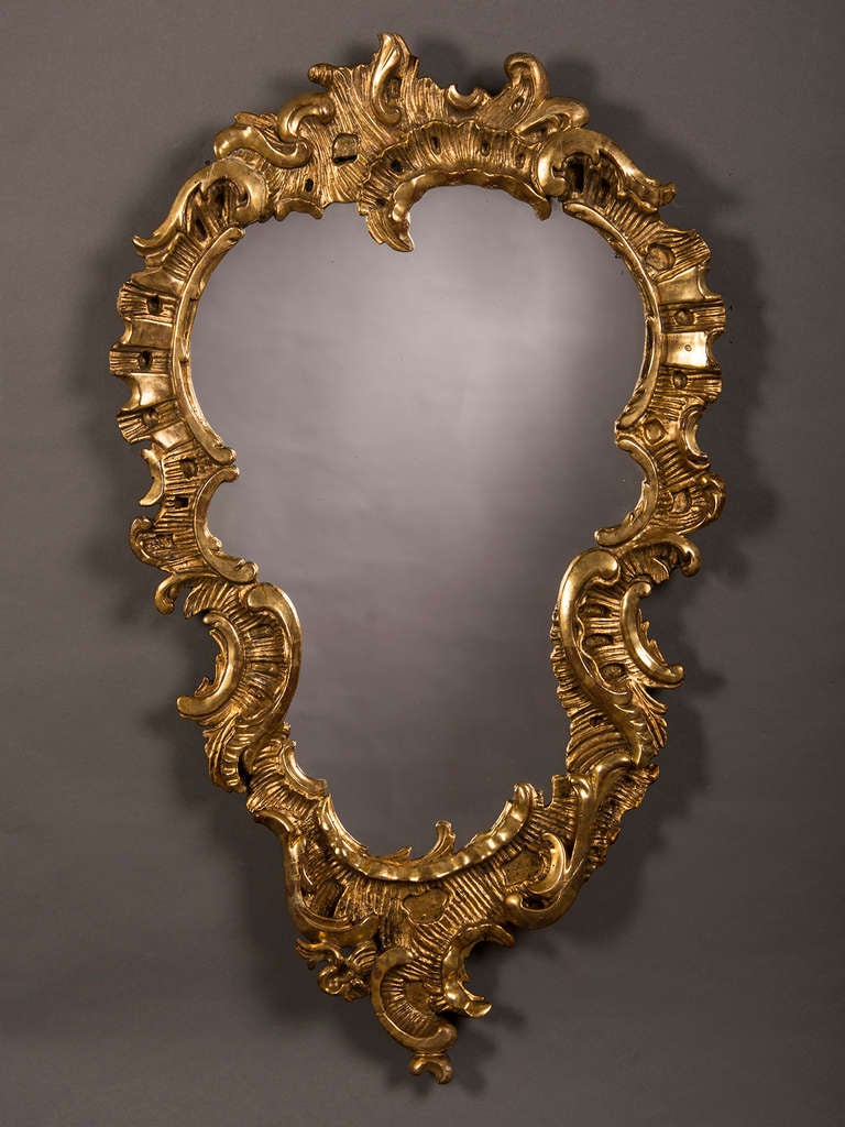 An antique French Louis XV period carved and gilded wood frame enclosing antique mirror glass circa 1760. Please note the lavish exuberance of the carved details of this frame. Scrolls and flourishes abound and reinforce the dramatic shape of the