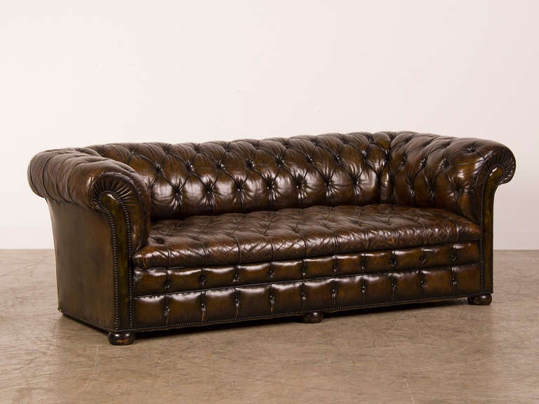 A handsome leather covered vintage Chesterfield sofa from England c. 1940. The elaborate detail on this example includes a double row of button tufting on the lower seat section as well as nail head trim that descends to the floor at each arm as