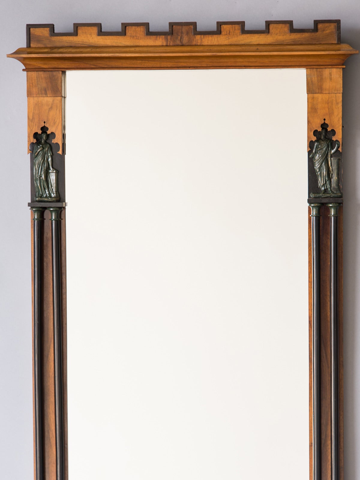 This elegant antique Austrian Biedermeier mirror circa 1825 features a pair of facing classical figures and highlights the importance of referencing the Greek and Roman past. The mirror frame is made of cherrywood with a decorative overlay of double