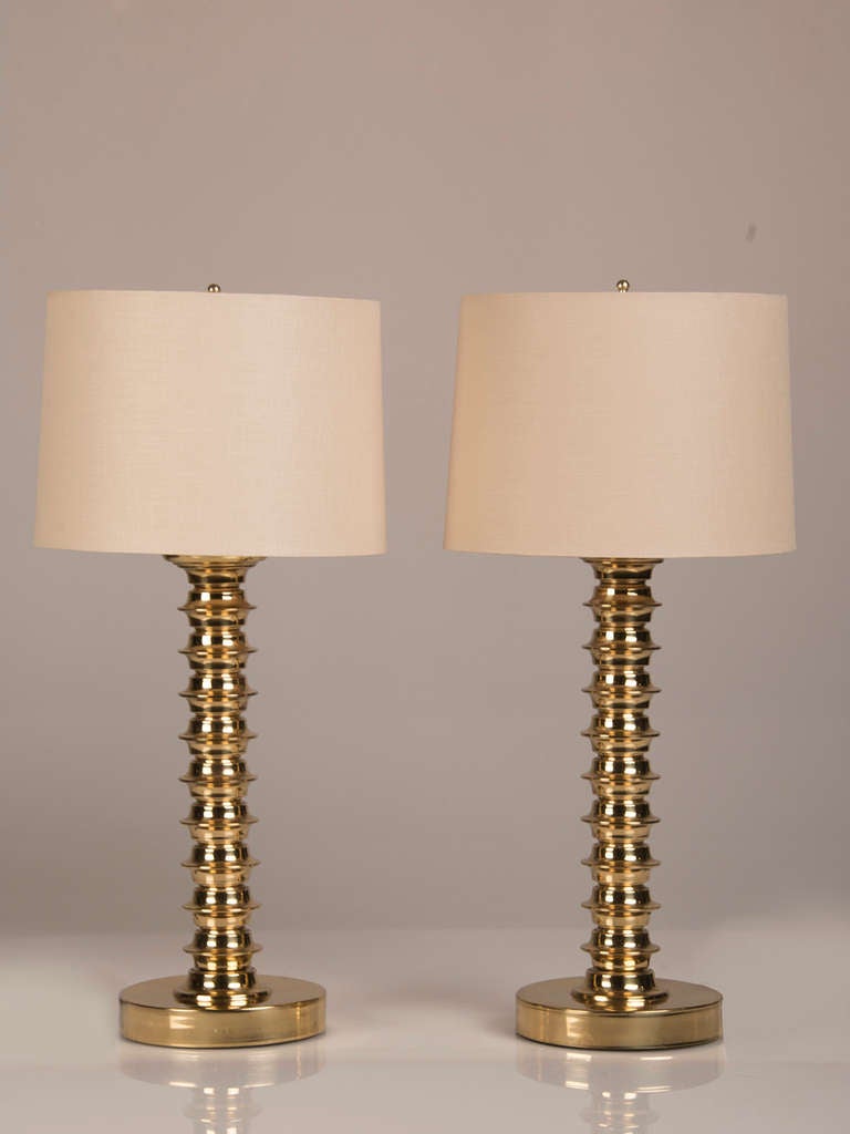 Pair of Tall Brass Bobbin Pattern Candlestick Lamps, England c.1890. These lamps possess a modern and graphic profile and have been topped with a linen drum shade to emphasize their striking shape and reflective finish. Each lamp has been fitted
