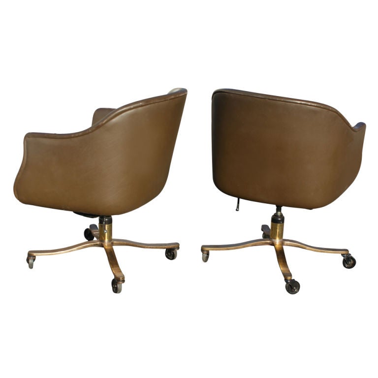 A pair of bucket chairs designed by Nicos Zographos and made by Zographos.  Brown leather with fabric seat cushions and four-star bronze bases on casters.  The chairs tilt and swivel.