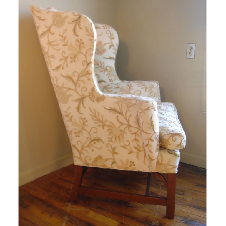 A Kittinger wingback lounge chair with a walnut base and down seat cushion.  The upholstery is crewel work in a floral design.