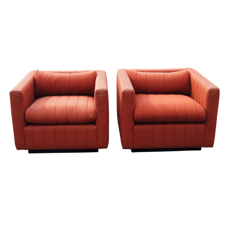A pair of mid century modern 87 Tuxedo lounge chairs designed by Nicos Zographos and made by Zographos.  Burnt orange upholstery with channels and black plinth bases.