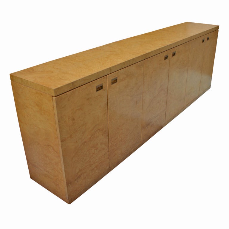 A mid century modern custon made credenza or cabinet in burled maple.  Three sets of doubled doors with inset brass hardware concealing shelved storage.  We have several of these pieces available.