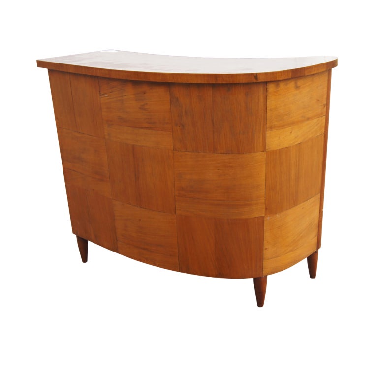 A mid century modern curved bar made of wood in a patchwork design with a wood grain laminate top.  Two open shelves, two drawers, and a lockable storage area.