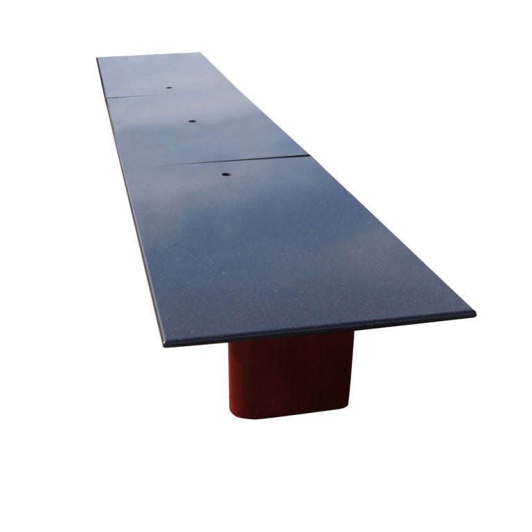 A modern styled conference table with a multi-pedestal mahogany base and Black granite top. The top features three apertures for cable management.
