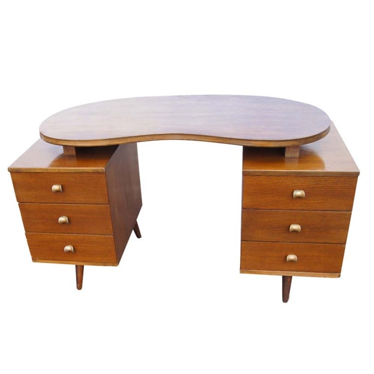 A mid century modern wooden desk and chair.  The desk with a floating kidney shaped top and double pedestal base with six drawers and brass hardware.  The chair measures 32