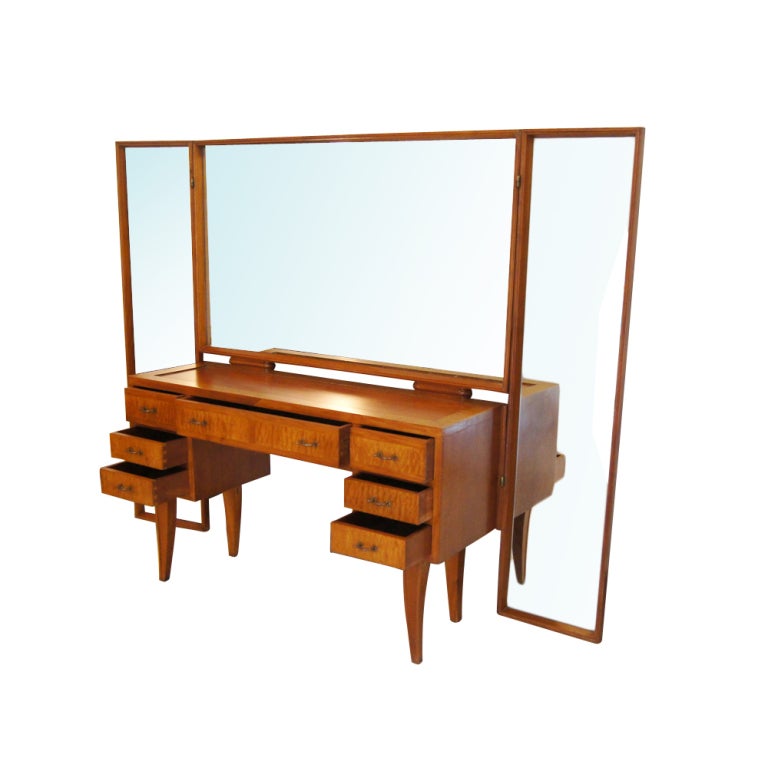 A nineteen forties vanity with a fixed center mirror and two hinged full-length side mirrors.  The case with seven drawers constructed of contrasting woods with brass hardware. 79
