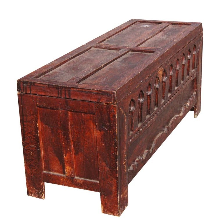 A rustic wooden chest carved with Moroccan designs with a reddish stain and removable top.