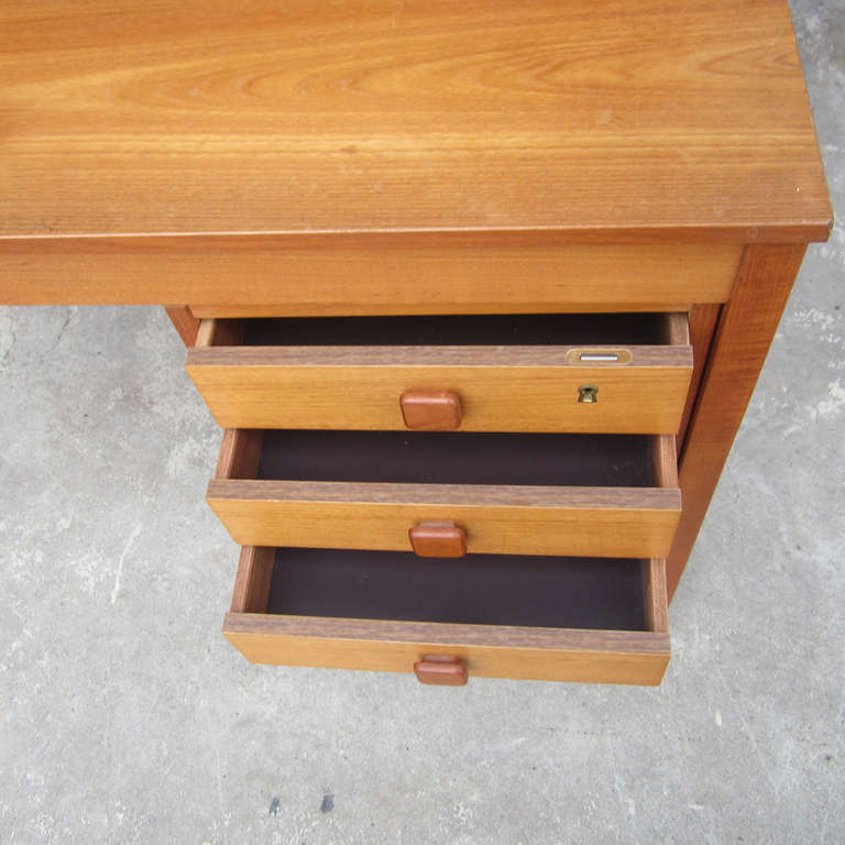 A small, Mid-Century Modern desk with three drawers, all of which have square wooden drawer pulls and one of which has a locking mechanism. A great schoolroom style small desk, perfect for any home or office.